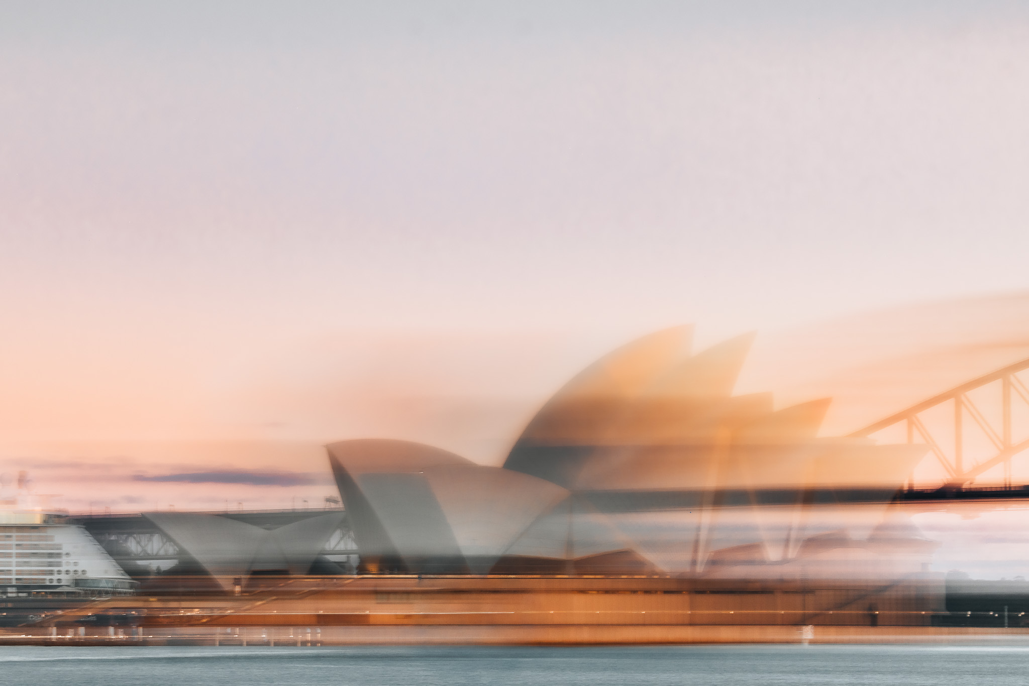 Intentional-camera-movement long exposure of the Sydney Opera House at dawn, the white sails smeared into vertical streaks of motion against a deep blue sky.